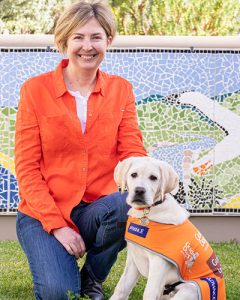 Woman kneeling on the grass with a small labrador in orange coat